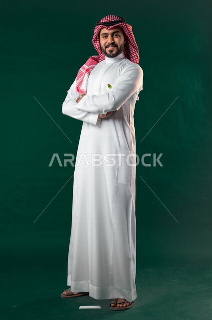 كروما، رجل عربي خليجي سعودي، ينظر إلى الكاميرا بأيدي متقاطعة، يرتدي الزي الخليجي السعودي التقليدي، الإحتفال باليوم الوطني السعودي، هوية اليوم الوطني السعودي 92، خلفية خضراء، يوم التأسيس السعودي، العيد الوطني السعودي، صورة بالطول الكامل