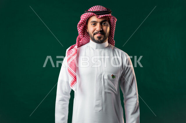 كروما، رجل عربي خليجي سعودي، ينظر إلى الكاميرا، يرتدي الزي الخليجي السعودي التقليدي، تعليق شعار اليوم الوطني لعام 2022 على صدره، الإحتفال باليوم الوطني السعودي، هوية اليوم الوطني السعودي 92، خلفية خضراء، يوم التأسيس السعودي