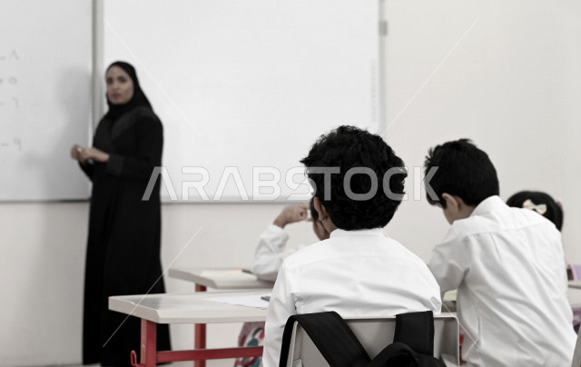 معلمة عربية سعودية خليجية تقوم بشرح الدروس لطلاب المرحلة الإبتدائية في الفصل , أهداف التربية والتعليم بالمناهج المقررة للطلاب والطالبات في المملكة العربية السعودية .