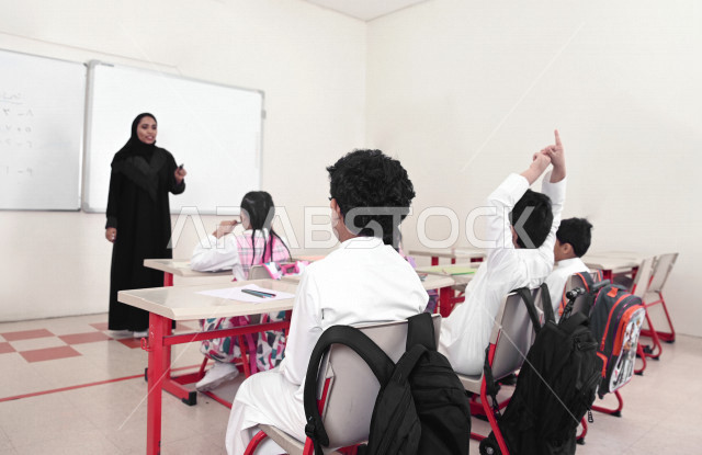 معلمة عربية سعودية خليجية تقوم بشرح الدروس لطلاب المرحلة الإبتدائية في الفصل , أهداف التربية والتعليم بالمناهج المقررة للطلاب والطالبات في المملكة العربية السعودية .