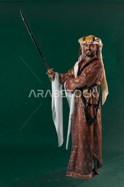 كروما لرجل عربي سعودي خليجي، يحمل السيف بيده, يرتدي الزي الشعبي التقليدي العريق, دقلة أهل المنطقه الوسطى مع المحزم والخنجر, الإحتفال باليوم الوطني، هوية اليوم الوطني السعودي 92، أزياء سعودية تراثية، يوم التأسيس، صورة الجسم بالطول الكامل, خلفيه خضراء