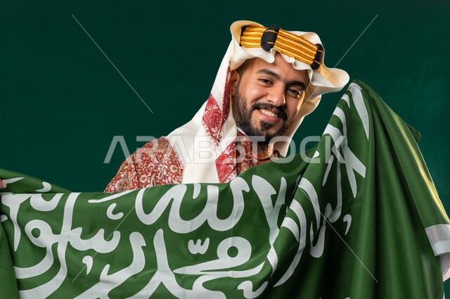 كروما لرجل عربي سعودي خليجي، يحمل علم السعوديه, يرتدي الزي الشعبي التقليدي العريق, دقلة أهل المنطقه الوسطى, الإحتفال باليوم الوطني السعودي، هوية اليوم الوطني السعودي 92، أزياء سعودية تراثية، يوم التأسيس السعودي، العيد الوطني السعودي, خلفيه خضراء