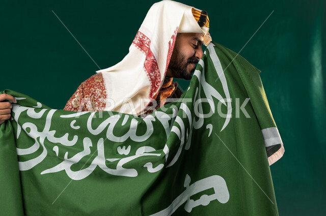 كروما لرجل عربي سعودي خليجي، يحمل علم السعوديه, يرتدي الزي الشعبي التقليدي العريق, دقلة أهل المنطقه الوسطى, الإحتفال باليوم الوطني السعودي، هوية اليوم الوطني السعودي 92، أزياء سعودية تراثية، يوم التأسيس السعودي، العيد الوطني السعودي, خلفيه خضراء