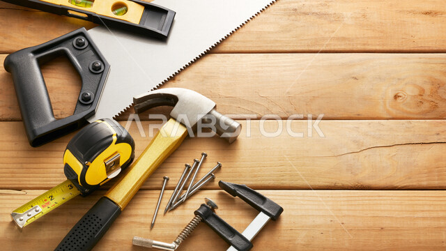 صورة مقربة لمجموعة من ادوات النجارة، شاكوش ومسامير، منشار خشبي، خلفية خشب