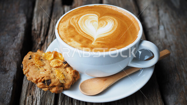 صورة مقربة لفنجان القهوة برغوة كثيفة مع رقاقة البسكويت الهشة مصورة على سطح خشبي ، مشروب الكابتشينو الساخن ، قهوة اسبريسو ، مشروبات ساخنة لذيذة ، فنجان القهوة الساخن ، كوكيز ، عرض فنّي للقهوة ، فن التصوير بشكل إحترافي