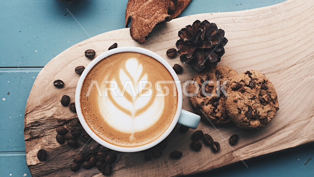 صورة مقربة لفنجان القهوة برغوة كثيفة مع رقائق البسكويت بالشوكولاته وحبوب البن المتناثرة مصورة على سطح خشبي ، مشروب الكابتشينو الساخن ، قهوة اسبريسو ، مشروبات ساخنة لذيذة ، فنجان القهوة الساخن ، كوكيز ، عرض فنّي للقهوة ، فن التصوير بشكل إحترافي