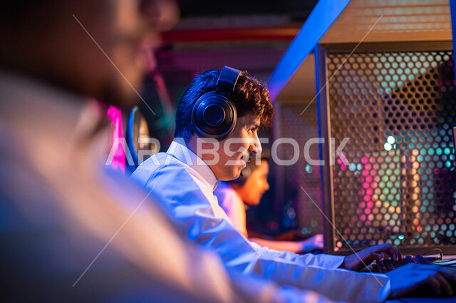 Young Arab Gulf Saudi teens in an electronic game store, wearing a headset and playing electronic video games, gestures indicating integration and interaction, recreational activities, computer entertainment, spending leisure time playing video games with