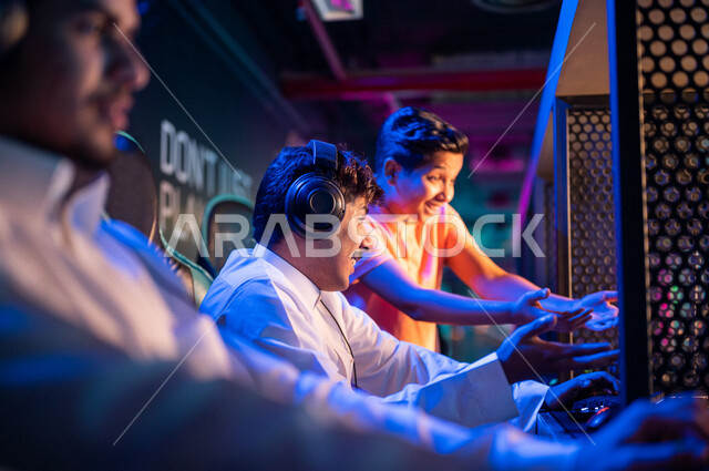 Young Arab Gulf Saudi teens in an electronic game store, wearing a headset and playing electronic video games, gestures indicating integration and interaction, recreational activities, computer entertainment, spending leisure time playing video games with