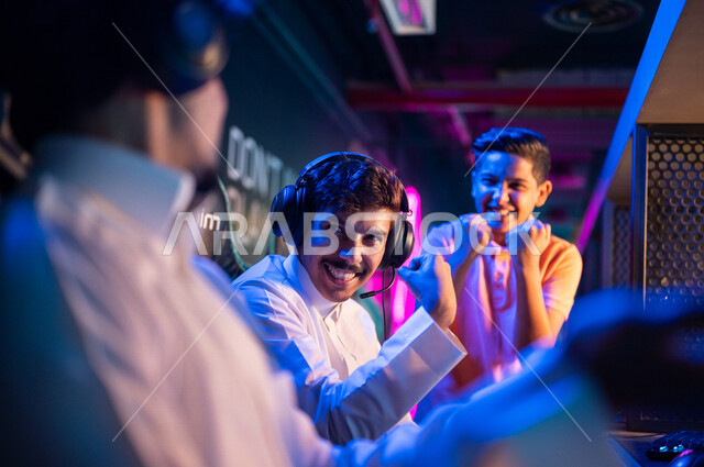 Young Arab Gulf Saudi teens in an electronic game store, wearing a headset and playing electronic video games, gestures indicating integration and interaction, recreational activities, computer entertainment, spending leisure time playing video games with