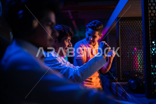 Arab youth Gulf Saudi teenagers in the electronic games store, wearing a headset and playing electronic video games, gestures indicating winning and happiness in the challenge, recreational activities, computer entertainment games, spending leisure time p