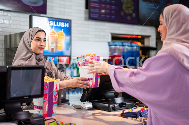 إمرأه عربيه سعوديه خليجيه تبيع المأكولات والمشروبات في ردهة الإستقبال داخل السينما، تسليم الفشار للزبائن, الإستعداد للدخول الى صالة العرض، مشاهدة الأفلام والعروض المسرحية، سينما ومسرح، أنشطه ترفيهيه