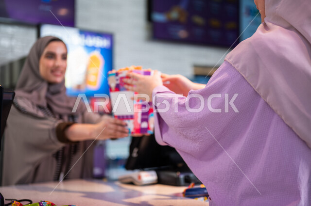  تصوير مقرب لإمرأه عربيه سعوديه خليجيه تبيع المأكولات والمشروبات في ردهة الإستقبال داخل السينما، تسليم الفشار للزبائن, الإستعداد للدخول الى صالة العرض، مشاهدة الأفلام والعروض المسرحية، سينما ومسرح، أنشطه ترفيهيه