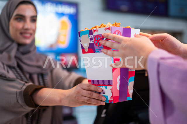  تصوير مقرب لإمرأه عربيه سعوديه خليجيه تبيع المأكولات والمشروبات في ردهة الإستقبال داخل السينما، تسليم الفشار للزبائن, الإستعداد للدخول الى صالة العرض، مشاهدة الأفلام والعروض المسرحية، سينما ومسرح، أنشطه ترفيهيه