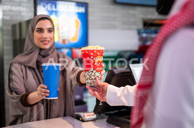  تصوير مقرب لإمرأه عربيه سعوديه خليجيه تبيع المأكولات والمشروبات في ردهة الإستقبال داخل السينما، تسليم المشروبات والفشار للزبائن, الإستعداد للدخول الى صالة العرض، مشاهدة الأفلام والعروض المسرحية، سينما ومسرح، أنشطه ترفيهيه