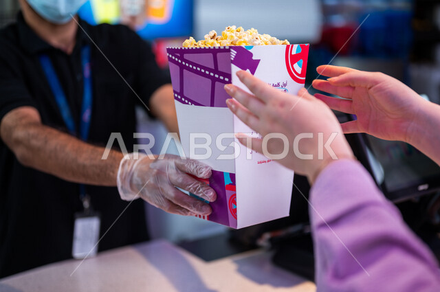  تصوير مقرب لرجل  يبيع الفوشار للزبائن في ردهة الإستقبال داخل السينما، إستلام الفوشار, الإستعداد للدخول الى صالة العرض، قضاء أوقات ممتعة، مشاهدة الأفلام والعروض المسرحية، سينما ومسرح، أنشطه ترفيهيه