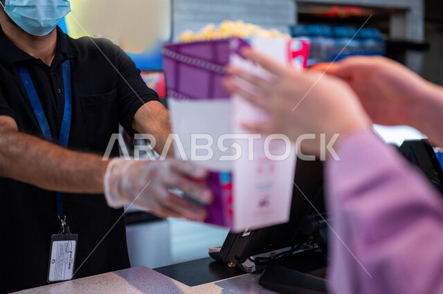  تصوير مقرب لرجل  يبيع الفوشار للزبائن في ردهة الإستقبال داخل السينما، إستلام الفوشار, الإستعداد للدخول الى صالة العرض، قضاء أوقات ممتعة، مشاهدة الأفلام والعروض المسرحية، سينما ومسرح، أنشطه ترفيهيه
