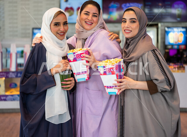 Gulf Arab female friends in the reception hall inside the cinema, looking at the camera, buying drinks and popcorn, getting ready to enter the showroom, spending fun times with friends, watching movies and theatrical performances, weekends, cinema and the
