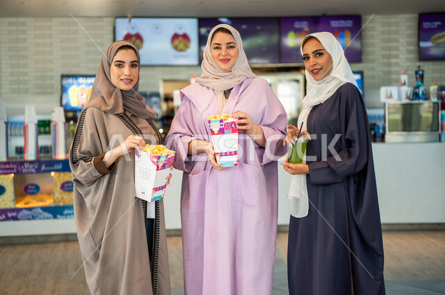 Gulf Arab female friends in the reception hall inside the cinema, looking at the camera, buying drinks and popcorn, getting ready to enter the showroom, spending fun times with friends, watching movies and theatrical performances, weekends, cinema and the