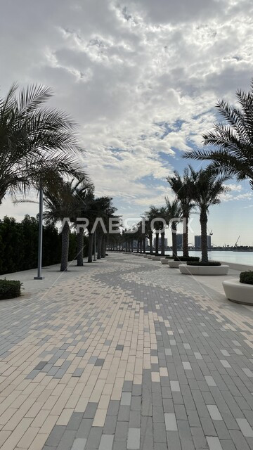 ممر مشاة مطل على كورنيش السيب في مسقط بعمان، الاشجار والنباتات الخضراء، السماء الملبدة بالغيوم، الواجهه البحرية على شاطئ السيب، مناظر طبيعية خلابة، اماكن سياحية