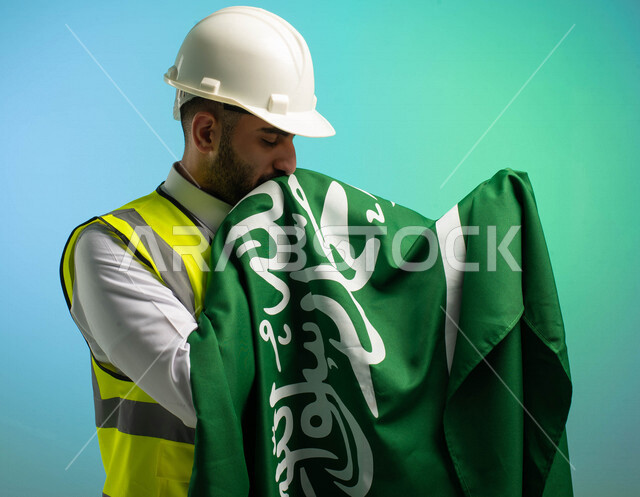 مهندس عربي خليجي سعودي يعمل في مجال الهندسة، يرتدي الخوذة وسترة الحماية، يقبل علم المملكة العربية السعودية، يحتفل باليوم الوطني السعودي، مهن ووظائف السعودية، العمالة السعودية، فرص عمل، مهنة الهندسة، اليوم الوطني السعودي، خلفية كروما