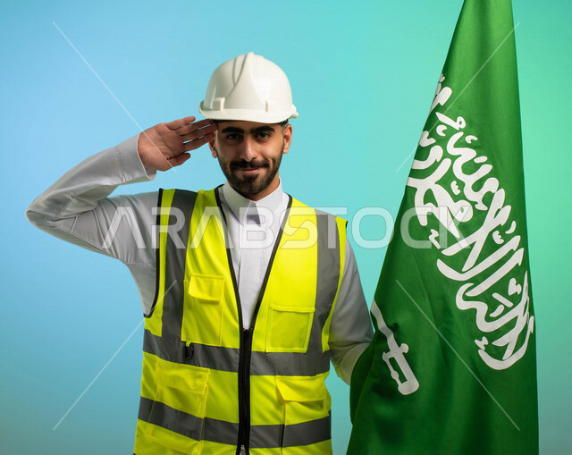 مهندس عربي خليجي سعودي يعمل في مجال الهندسة، يرتدي الخوذة وسترة الحماية، يحمل علم السعودية ويلقي تحية السلام الوطني، يحتفل باليوم الوطني، مهن ووظائف السعودية، العمالة السعودية، فرص عمل، مهنة الهندسة، اليوم الوطني السعودي، خلفية كروما