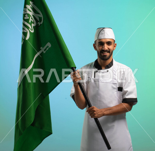 طاه وطباخ عربي خليجي سعودي يعمل في مجال فنون الطهي، يرتدي الزي الرسمي الخاص بمزاولة مهنة الشيف، يحمل علم المملكة العربية السعودية، يحتفل باليوم الوطني، مهن خدمات الأطعمة، العمالة السعودية، فرص عمل، مهنة طاهي الطعام، اليوم الوطني السعودي، خلفية كروما