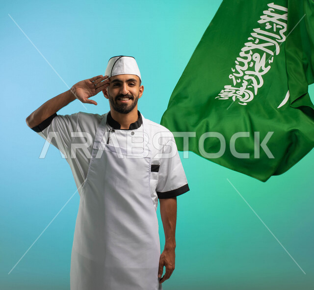 طاه وطباخ عربي خليجي سعودي يعمل في مجال فنون الطهي، يرتدي الزي الرسمي الخاص بمزاولة مهنة الشيف، يلقي تحية السلام لوطنه الحبيب، خلفية علم السعودية، مهن خدمات الأطعمة، العمالة السعودية، فرص عمل، مهنة طاهي الطعام، اليوم الوطني السعودي، خلفية كروما