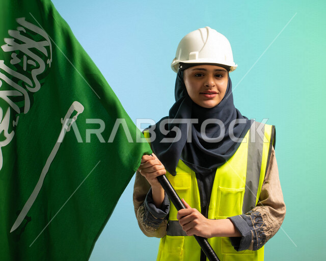 مهندسة عربية خليجية سعودية تعمل في مجال الهندسة، ترتدي الخوذة وسترة الحماية، مبتمسة وتنظر إلى الكاميرا، تحمل علم السعودية، تحتفل باليوم الوطني السعودي، مهن ووظائف السعودية، العمالة السعودية، فرص عمل، مهنة الهندسة، اليوم الوطني السعودي، خلفية كروما