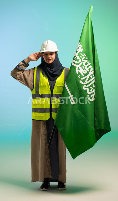 مهندسة عربية خليجية سعودية تعمل في مجال الهندسة، ترتدي الخوذة وسترة الحماية، تلقي تحية السلام لوطنها الحبيب بجانب علم السعودية، مهن ووظائف السعودية، العمالة السعودية، فرص عمل، مهنة الهندسة، اليوم الوطني السعودي، خلفية كروما، صورة بالطول الكامل