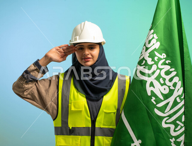 مهندسة عربية خليجية سعودية تعمل في مجال الهندسة، ترتدي الخوذة وسترة الحماية، تلقي تحية السلام لوطنها الحبيب بجانب علم المملكة العربية السعودية، مهن ووظائف السعودية، العمالة السعودية، فرص عمل، مهنة الهندسة، اليوم الوطني السعودي، خلفية كروما