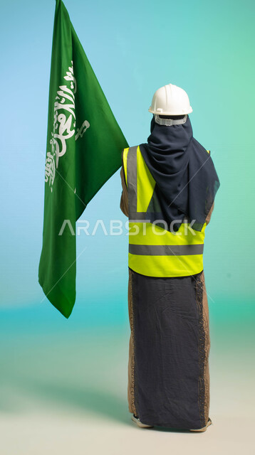 زاوية من الخلف، مهندسة عربية خليجية سعودية تعمل في مجال الهندسة، ترتدي الخوذة وسترة الحماية، تحمل علم السعودية، تحتفل باليوم الوطني، مهن ووظائف السعودية، العمالة السعودية، فرص عمل، مهنة الهندسة، اليوم الوطني السعودي، خلفية كروما، صورة بالطول الكامل