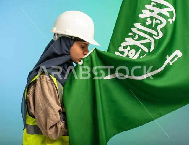 مهندسة عربية خليجية سعودية تعمل في مجال الهندسة، ترتدي الخوذة وسترة الحماية، تقبل علم المملكة العربية السعودية، تحتفل باليوم الوطني السعودي، مهن ووظائف السعودية، العمالة السعودية، فرص عمل، مهنة الهندسة، اليوم الوطني السعودي، خلفية كروما