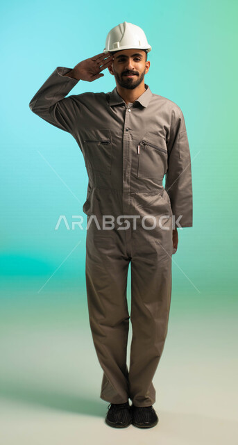 مهندس فني عربي خليجي سعودي يعمل في قطاع الإنشاءات، يرتدي خوذة الحماية، ينظر إلى الكاميرا ويلقي تحية السلام، مهن ووظائف سعودية، العمالة السعودية، فرص عمل، مهنة فني كهرباء، الأعمال والصيانة، خلفية كروما، صورة بالطول الكامل