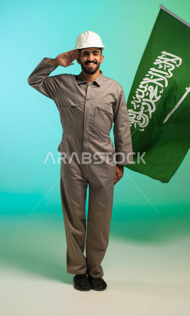 Saudi Arabian Gulf technical engineer working in the construction sector, saluting peace for his beloved country, background of Saudi flag, Saudi professions and jobs, Saudi labor, job opportunities, electrical technician profession, business and maintena