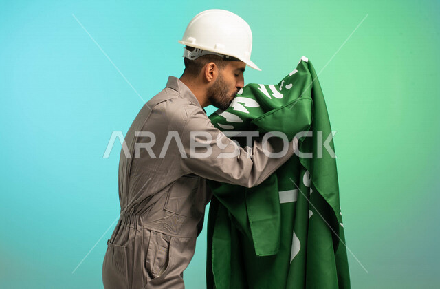 مهندس فني عربي خليجي سعودي يعمل في قطاع الإنشاءات، يرتدي خوذة الحماية، يقبل علم السعودية، يحتفل باليوم الوطني، مهن ووظائف سعودية، العمالة السعودية، فرص عمل، مهنة فني كهرباء، الأعمال والصيانة، اليوم الوطني السعودي، خلفية كروما