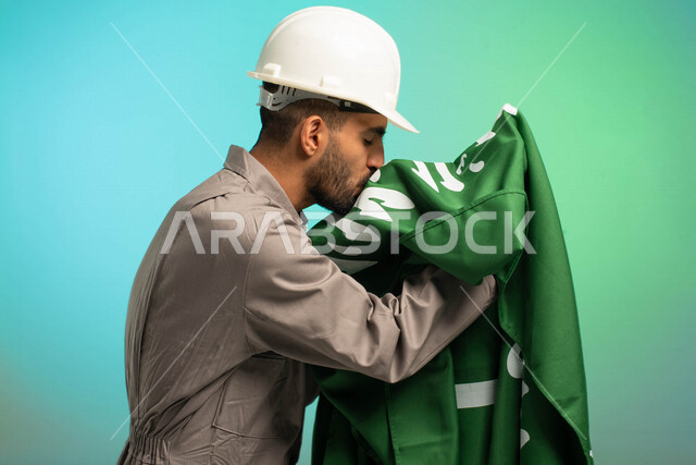 مهندس فني عربي خليجي سعودي يعمل في قطاع الإنشاءات، يرتدي خوذة الحماية، يقبل علم السعودية، يحتفل باليوم الوطني، مهن ووظائف سعودية، العمالة السعودية، فرص عمل، مهنة فني كهرباء، الأعمال والصيانة، اليوم الوطني السعودي، خلفية كروما