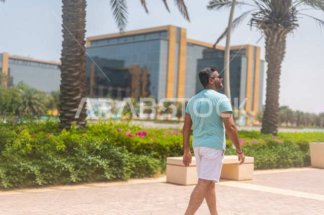 زاوية من الخلف لرجل عربي خليجي سعودي يقضي أوقات ممتعة بالتجول في كورنيش جدة، ممارسة رياضة المشي، واجهة جدة البحرية، أماكن سياحية ترفيهية بالسعودية، الإستجمام والتنزه، ممارسة نشاط المشي على ممشى كورنيش جدة السياحي، أنشطة ترفيهية في جدة