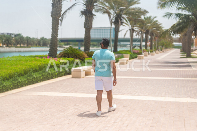 زاوية من الخلف لرجل عربي خليجي سعودي يقضي أوقات ممتعة بالتجول في كورنيش جدة، ممارسة رياضة المشي، واجهة جدة البحرية، أماكن سياحية ترفيهية بالسعودية، الإستجمام والتنزه، ممارسة نشاط المشي على ممشى كورنيش جدة السياحي، أنشطة ترفيهية في جدة