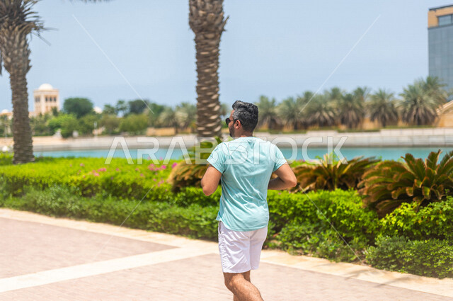 زاوية من الخلف لرجل عربي خليجي سعودي يمارس الرياضة الصباحية على كورنيش جدة، ممارسة رياضة الجري على ممشى كورنيش جدة السياحي، واجهة جدة البحرية، أماكن سياحية ترفيهية بالسعودية، المحافظة على اللياقة والصحة الجيدة، أنشطة ترفيهية في جدة