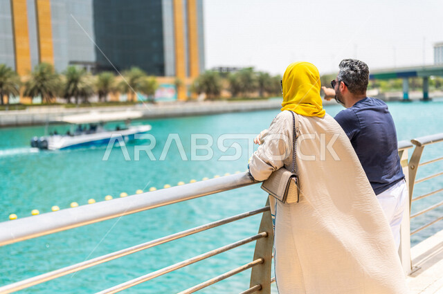 زاوية من الخلف لزوجان عربيان خليجيان سعوديان يقضيان أوقات ممتعة على كورنيش جدة، كورنيش جدة السياحي، أماكن سياحية ترفيهية بالمملكة العربية السعودية، الإستجمام والتنزه في الهواء الطلق، نشاطات ترفيهية بجدة، أسرة سعودية