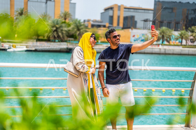 A Saudi Arabian Gulf couple spending fun times on the Jeddah Corniche, taking memorial selfies using a mobile phone, expressions of happiness, Jeddah Tourist Corniche, recreational tourist places in Saudi Arabia, recreation and hiking, recreational activi