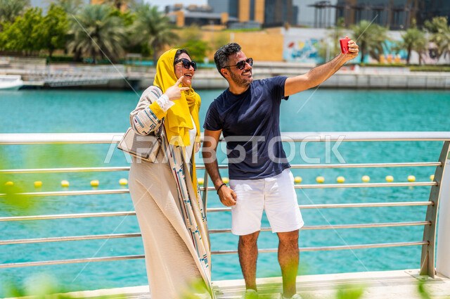 زوجان عربيان خليجيان سعوديان يقضيان أوقات ممتعة على كورنيش جدة، إلتقاط صور سيلفي تذكاريه بإستخدام الهاتف المحمول، تعابير تدل على السعادة، كورنيش جدة السياحي، أماكن سياحية ترفيهية بالسعودية، الإستجمام والتنزه، نشاطات ترفيهية بجدة، أسرة سعودية