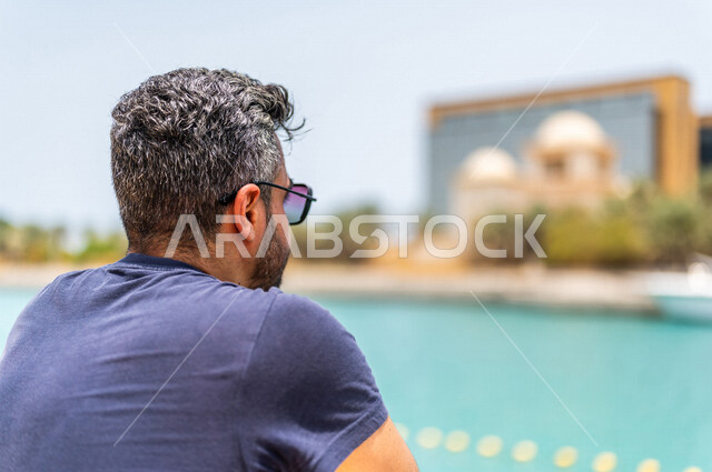 زاوية من الخلف لرجل عربي خليجي سعودي يقضي أوقات ممتعة على كورنيش جدة، واجهة جدة البحرية، أماكن سياحية ترفيهية بالمملكة العربية السعودية، الإستجمام والتنزه في الهواء الطلق، كورنيش جدة السياحي، خلفية ضبابية، أنشطة ترفيهية في جدة