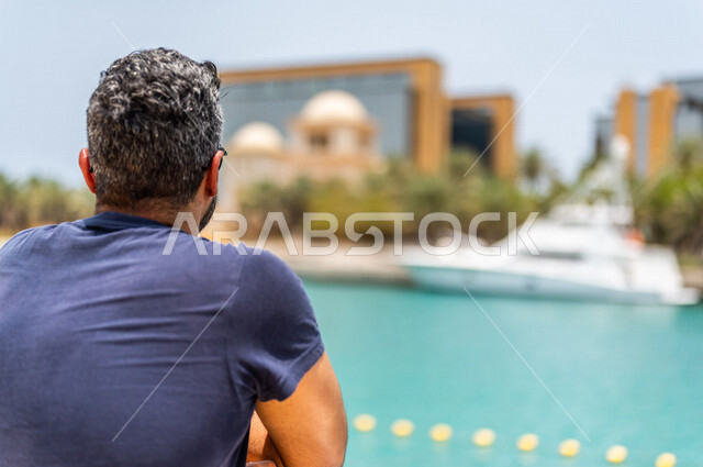 An angle from the back of a Saudi Arabian Gulf man spending fun times on the Jeddah Corniche, Jeddah Waterfront, recreational tourist places in Saudi Arabia, recreation and outdoor walks, Jeddah Tourist Corniche, foggy background, recreational activities 