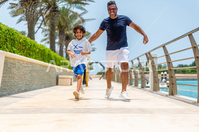 رجل عربي خليجي سعودي يقضي وقت ممتع برفقة إبنه على ممشى كورنيش جدة، كورنيش جدة السياحي، واجهة جدة البحرية، أماكن سياحية ترفيهية بالمملكة العربية السعودية، نشاطات ترفيهية مع الأبناء، تحدي وسباق الجري