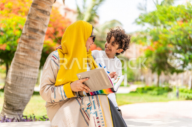 مرأة عربية خليجية سعودية تقضي وقت ممتع برفقة إبنها في إحدى الحدائق السياحية الترفيهية في المملكة العربية السعودية، تعابير تدل على السعادة، تحمل بيدها كتاب، قضاء أوقات عائلية ممتعة، مفهوم الأسرة السعيدة، جلسات هادئة، خلفية الطبيعة، حدائق عامة
