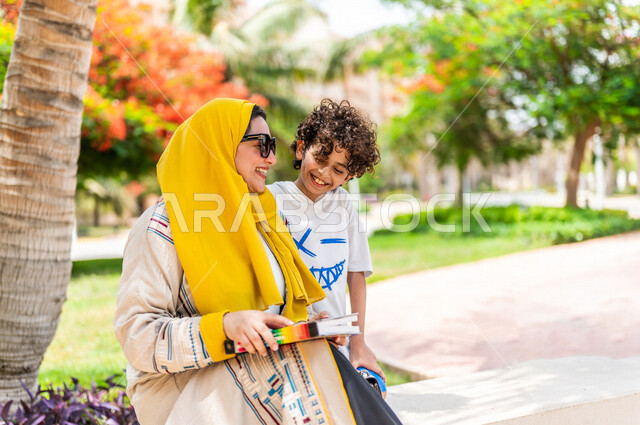مرأة عربية خليجية سعودية تقضي وقت ممتع برفقة إبنها في إحدى الحدائق السياحية الترفيهية في المملكة العربية السعودية، تعابير تدل على السعادة، تحمل بيدها كتاب، قضاء أوقات عائلية ممتعة، مفهوم الأسرة السعيدة، جلسات هادئة، خلفية الطبيعة، حدائق عامة