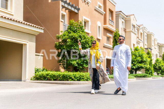 زوجان عربيان خليجيان سعوديان يتجولان في الأحياء السكنية الراقية بالسعودية، ينظران إلى العمارات السكنية، تشير الزوجة بإصبعها لأعلى، كمباوند سكني، مجمع سكني، الإسكان العائلي بالسعودية، تصاميم هندسية معمارية حديثة، أسرة سعودية، جودة الحياة