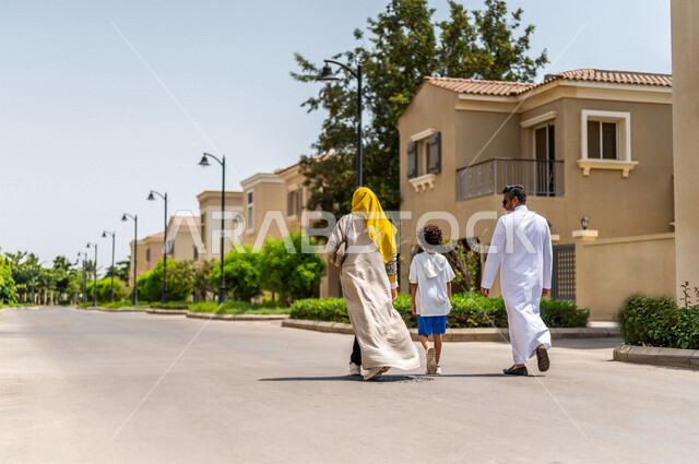 زاوية من الخلف لعائلة عربية خليجية سعودية تتجول في الأحياء السكنية الراقية بالسعودية، كمباوند سكني، فلل سكنية، مجمع سكني، الإسكان العائلي في السعودية، أجواء عائلية سعيدة، أسرة سعودية، جودة الحياة
