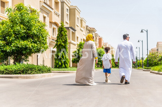 زاوية من الخلف لعائلة عربية خليجية سعودية تتجول في الأحياء السكنية الراقية بالسعودية، كمباوند سكني، فلل سكنية، مجمع سكني، الإسكان العائلي في السعودية، أجواء عائلية سعيدة، أسرة سعودية، جودة الحياة